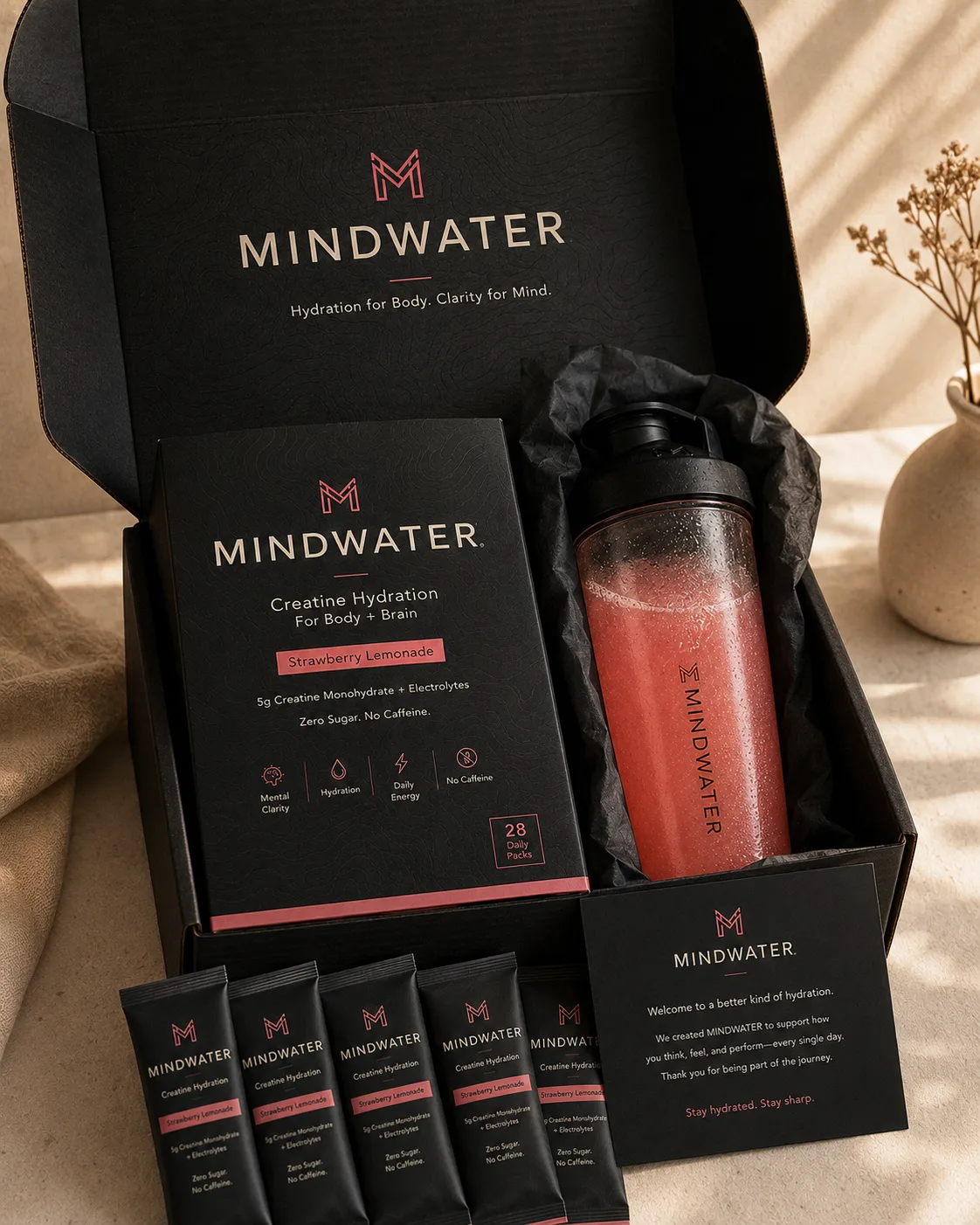 Open premium shipping box revealing the MINDWATER product box, glass shaker wrapped in tissue, welcome card, and daily packs